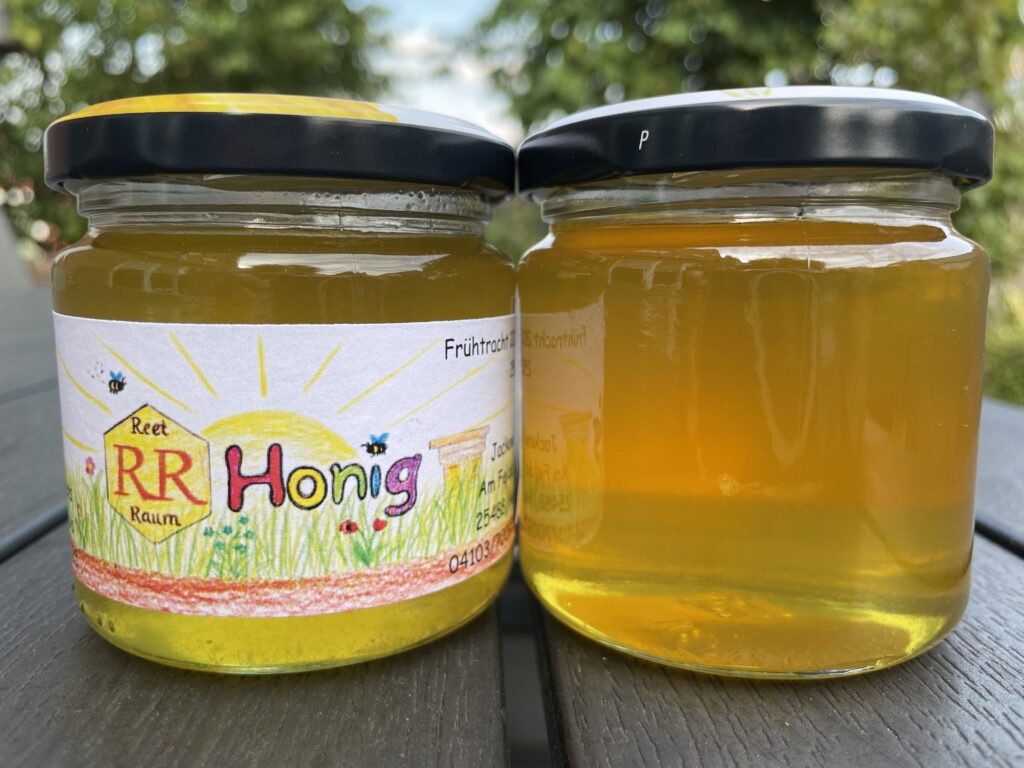 Zwei Honiggläser 250g vom Reet-Raum-Honig. Einmal von vorne mit Etikett und einmal von hinten.
